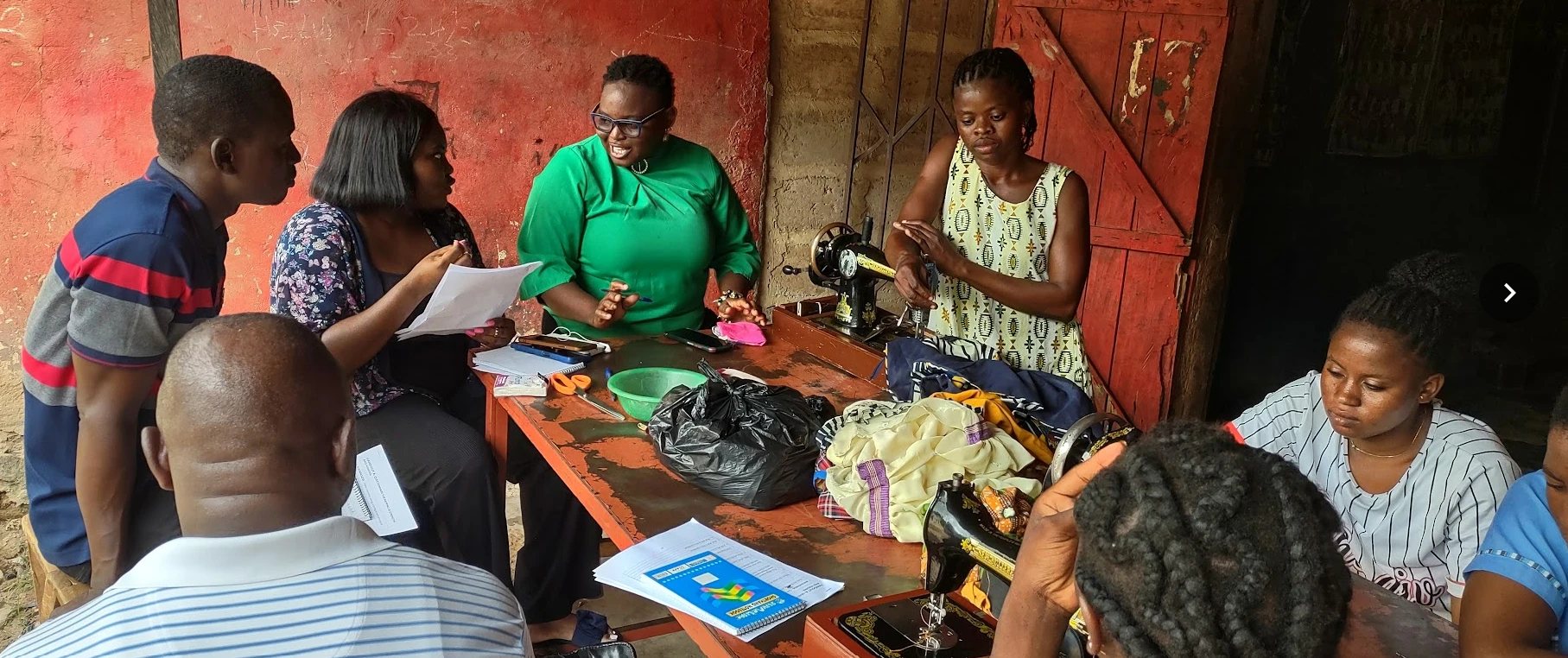 Survey team with questionnaires interviewing women at sewing machines in a tailoring workshop