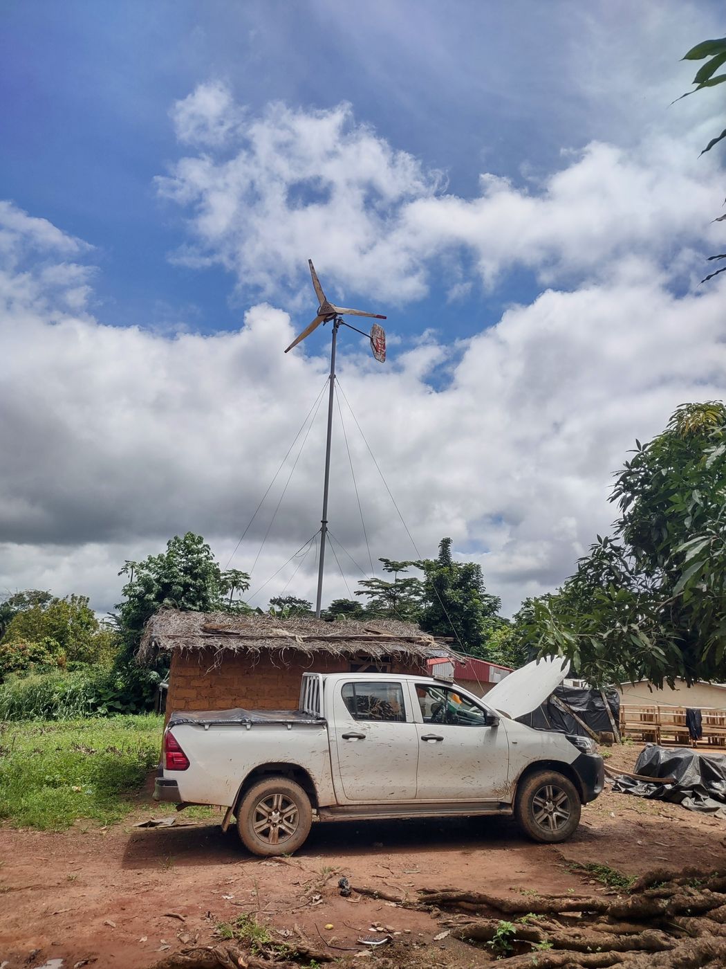 A wind turbine installed beside a village house, with a pickup truck in front